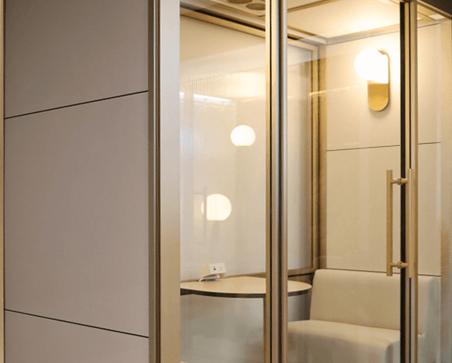 Custom privacy pod featuring a gold anodized frame, reeded glass back wall, and custom wall sconce lighting in soft neutral tones.