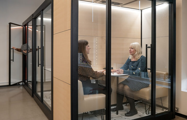 Two professionals sitting in a custom wood-paneled privacy pod at CAA's Ottawa headquarters, providing a quiet, focused space in an open office environment.